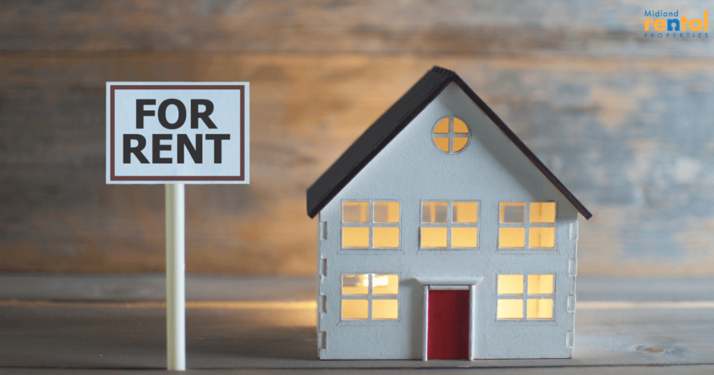 For rent sign next to a model house with glowing windows, symbolizing rental property availability.